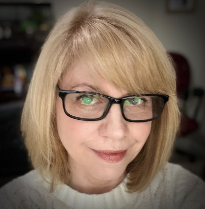 Maureen, smiling, in glasses and a cream sweater